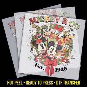 May include: A DTF transfer featuring Mickey Mouse and friends in a festive wreath design. The image includes Mickey, Minnie, Donald, Daisy, Goofy, and Pluto, with the text "Mickey & Co. Est. 1928". The design has a red bow and red and white striped scarves.