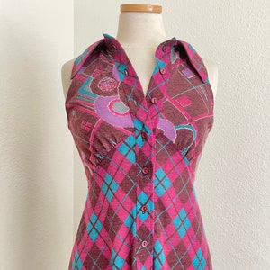 May include: A sleeveless maxi dress with a button-up front and a collar. The dress is made of a pink and blue patterned fabric with a diamond pattern.