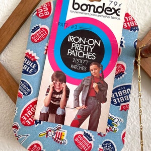 May include: A vintage package of iron-on patches featuring two children. The package is pink and blue with the text "Iron-On Pretty Patches 2(5"x7") Approx Patches" and the brand name "bondex".