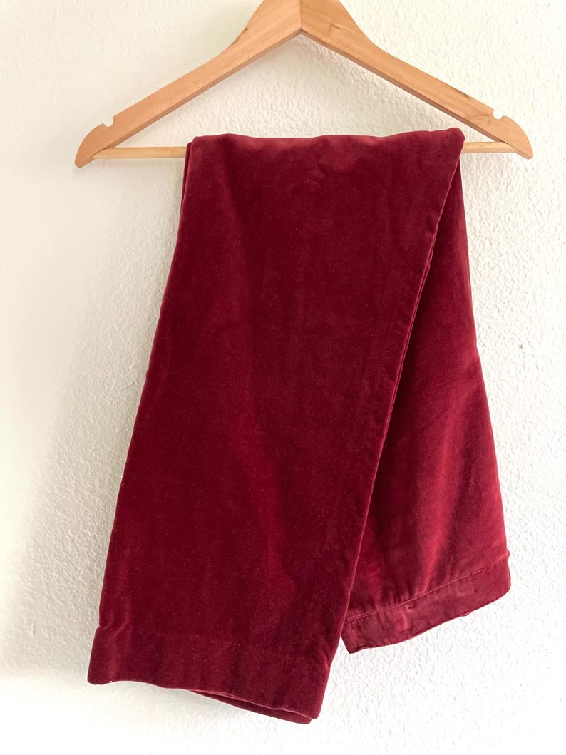 Puede incluir: Un pantal&oacute;n de terciopelo burdeos colgado de una percha de madera.