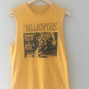 May include: A yellow sleeveless shirt with a black graphic print of a band called "The Hellacopters" with the text "Rock & Roll" and a cartoon image of a person playing a guitar.