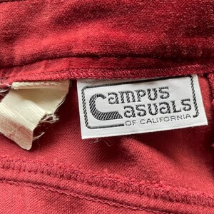 Puede incluir: Primer plano de una tela de pana roja con una etiqueta blanca que dice "Campus Casuals of California".