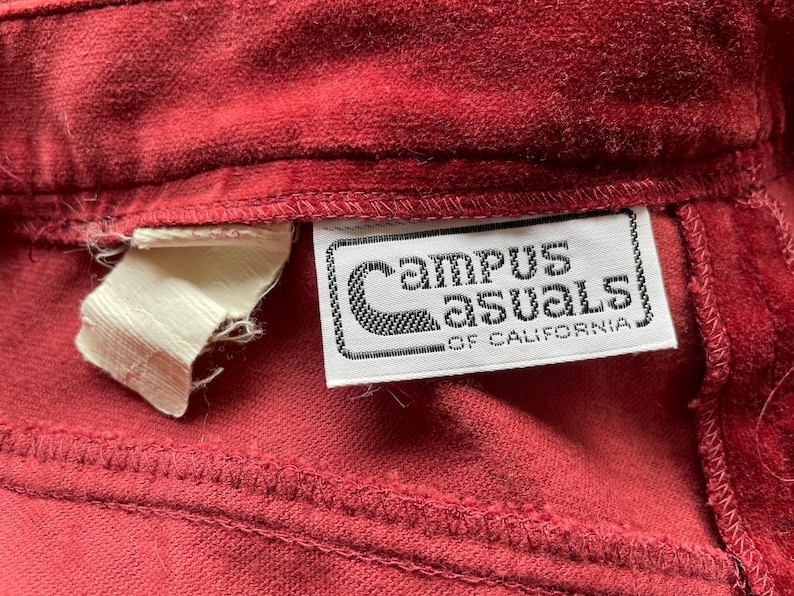 Puede incluir: Primer plano de una tela de pana roja con una etiqueta blanca que dice "Campus Casuals of California".