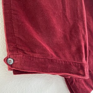 Puede incluir: Un pantal&oacute;n de terciopelo burdeos con un bot&oacute;n en la costura lateral.