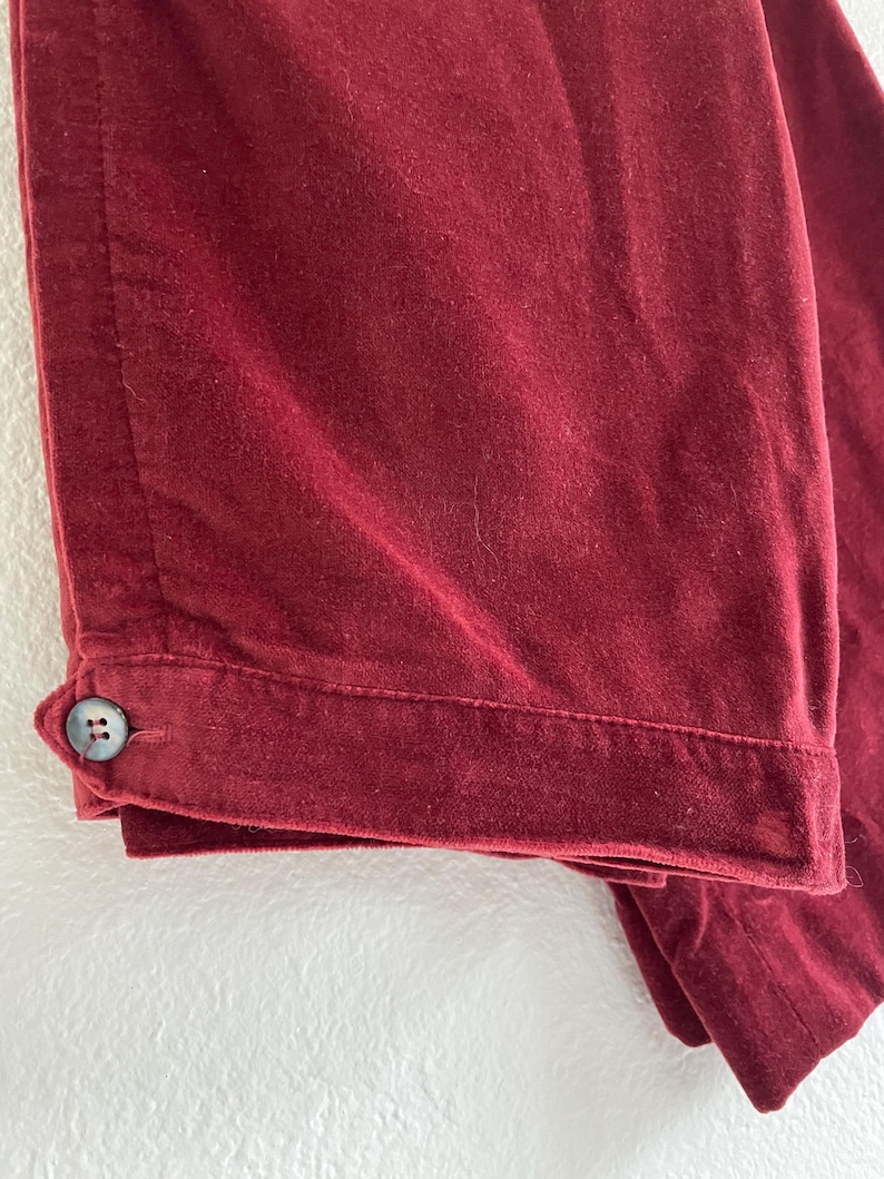 Puede incluir: Un pantal&oacute;n de terciopelo burdeos con un bot&oacute;n en la costura lateral.