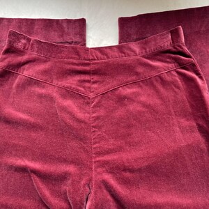 Puede incluir: Un pantal&oacute;n de terciopelo burdeos de cintura alta y pierna recta.