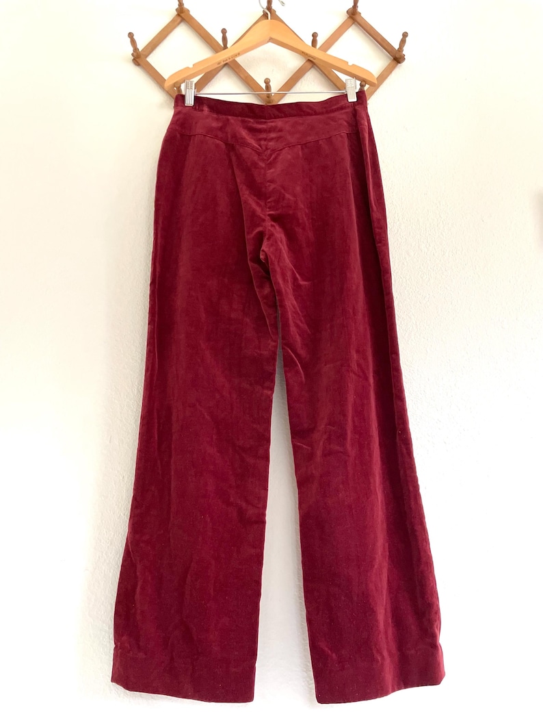 Puede incluir: Un par de pantalones de pierna ancha en color burdeos oscuro. Los pantalones est&aacute;n hechos de una tela suave y aterciopelada y tienen una cintura alta.