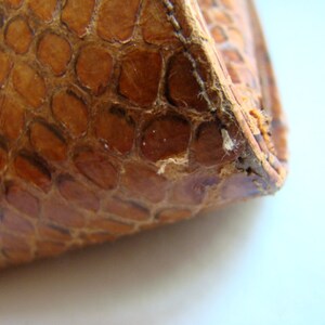 Puede incluir: Primer plano de la esquina de un bolso o cartera de cuero marr&oacute;n con un patr&oacute;n texturizado de piel de serpiente.