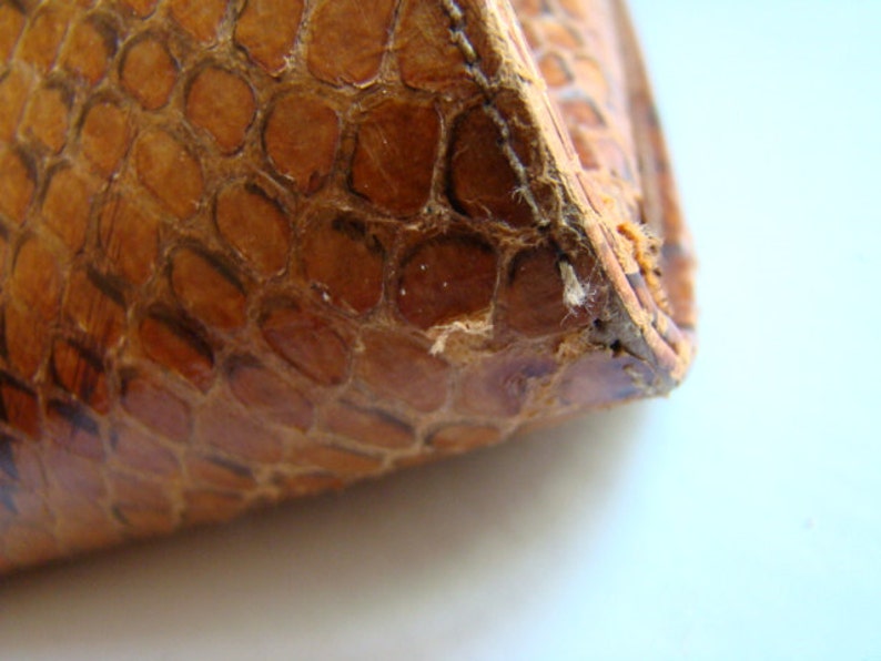 Puede incluir: Primer plano de la esquina de un bolso o cartera de cuero marr&oacute;n con un patr&oacute;n texturizado de piel de serpiente.