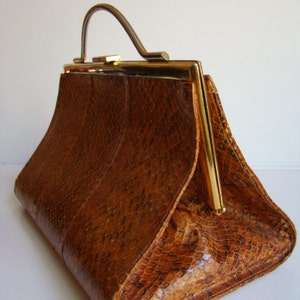 Puede incluir: Un bolso de cuero marr&oacute;n con un cierre dorado y un asa dorada. El bolso tiene un patr&oacute;n texturizado y escamoso.