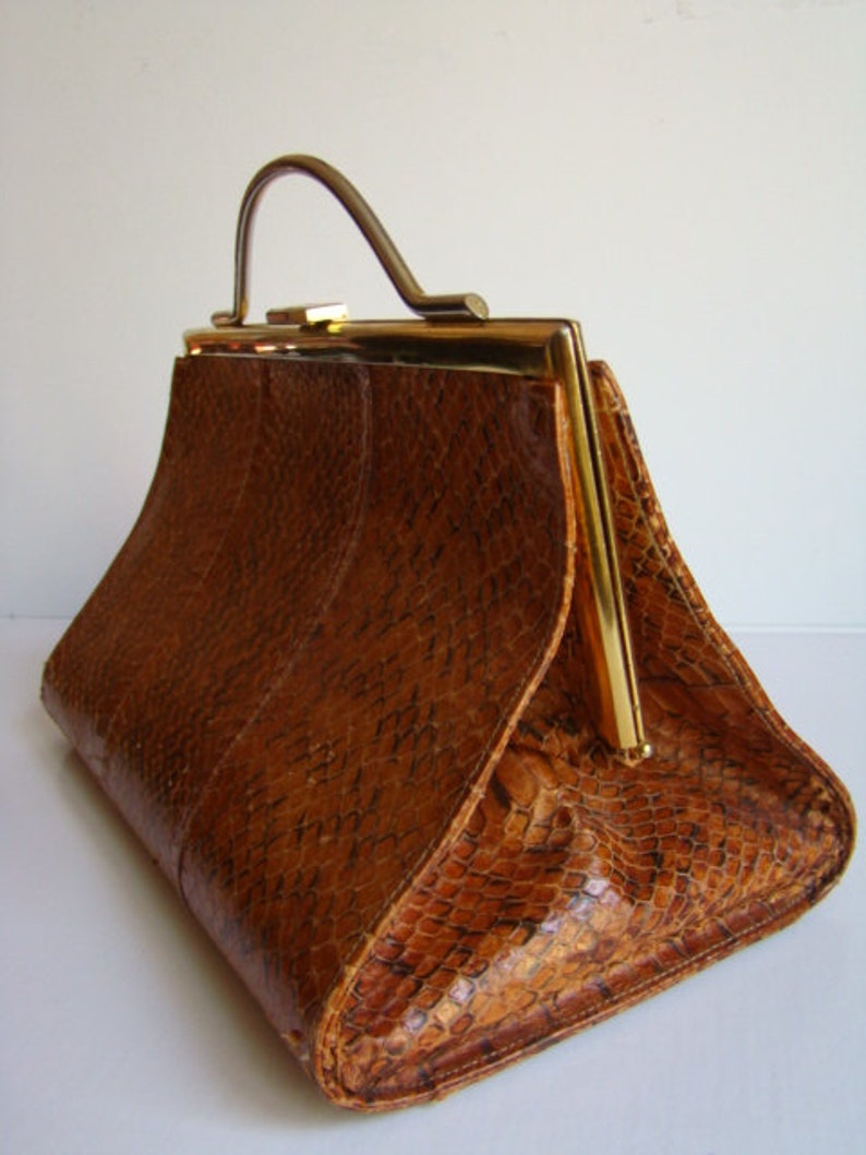 Puede incluir: Un bolso de cuero marr&oacute;n con un cierre dorado y un asa dorada. El bolso tiene un patr&oacute;n texturizado y escamoso.