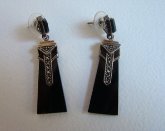 May include: A pair of Art Deco-style earrings. Each earring features a black, rectangular onyx stone with a silver-toned metal top adorned with marcasite stones. The earrings have a post-back closure.