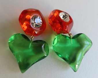May include: A pair of statement earrings featuring a green heart-shaped charm and a red, faceted, octagonal charm with a clear rhinestone.