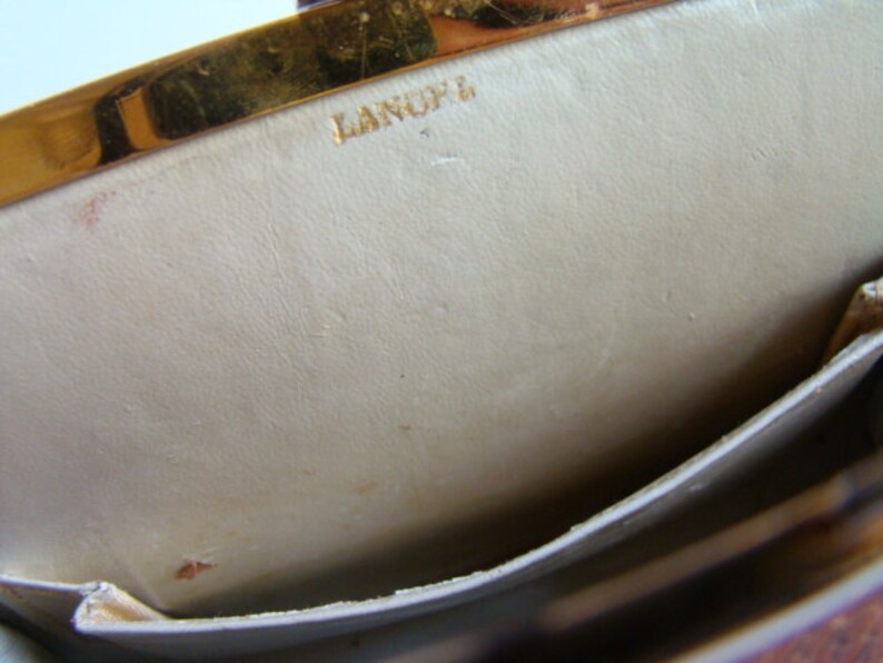 Puede incluir: El interior de un bolso de cuero beige claro con un cierre de metal dorado. El bolso tiene un peque&ntilde;o bolsillo en el interior y el nombre de la marca "LANOFF" est&aacute; estampado en dorado en la parte delantera.