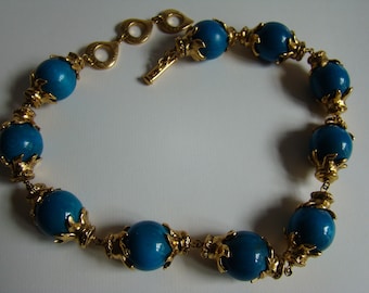 May include: A gold necklace with a chain and large turquoise blue beads. Each bead is surrounded by a gold decorative design.