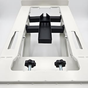 Peut inclure: Une structure de cadre en métal blanc dotée d'un composant central noir réglable avec un plateau rectangulaire. Le cadre comprend deux boutons de réglage noirs en forme d'étoile avec des boulons métalliques filetés pour le mécanisme.