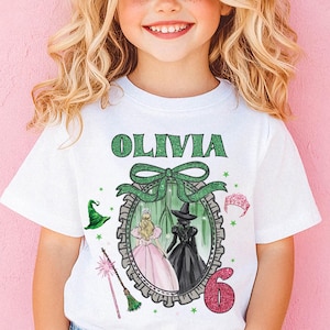 A young girl with curly blonde hair wearing a white t-shirt with a graphic design and a bow on her head, smiling at the camera.