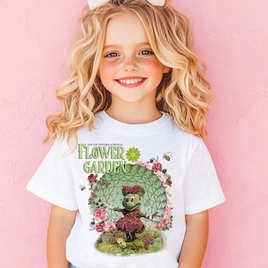 A young girl with curly blonde hair wearing a white t-shirt with a floral design and a bow in her hair, smiling at the camera.