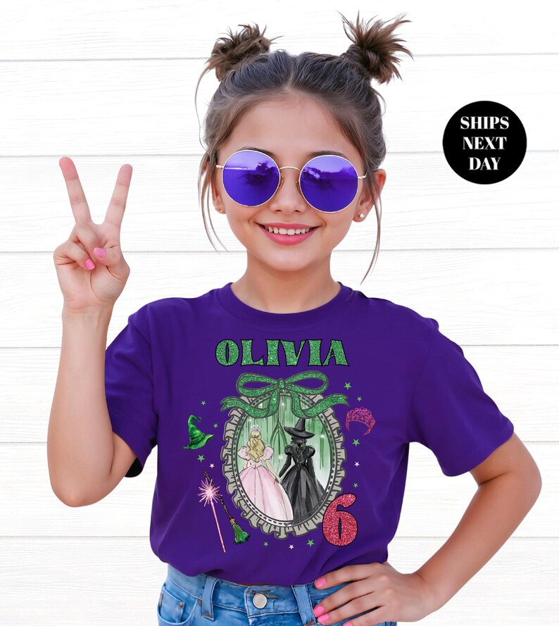 A young girl wearing a purple t-shirt with a graphic design and the text "Olivia 6" is smiling and making a peace sign.