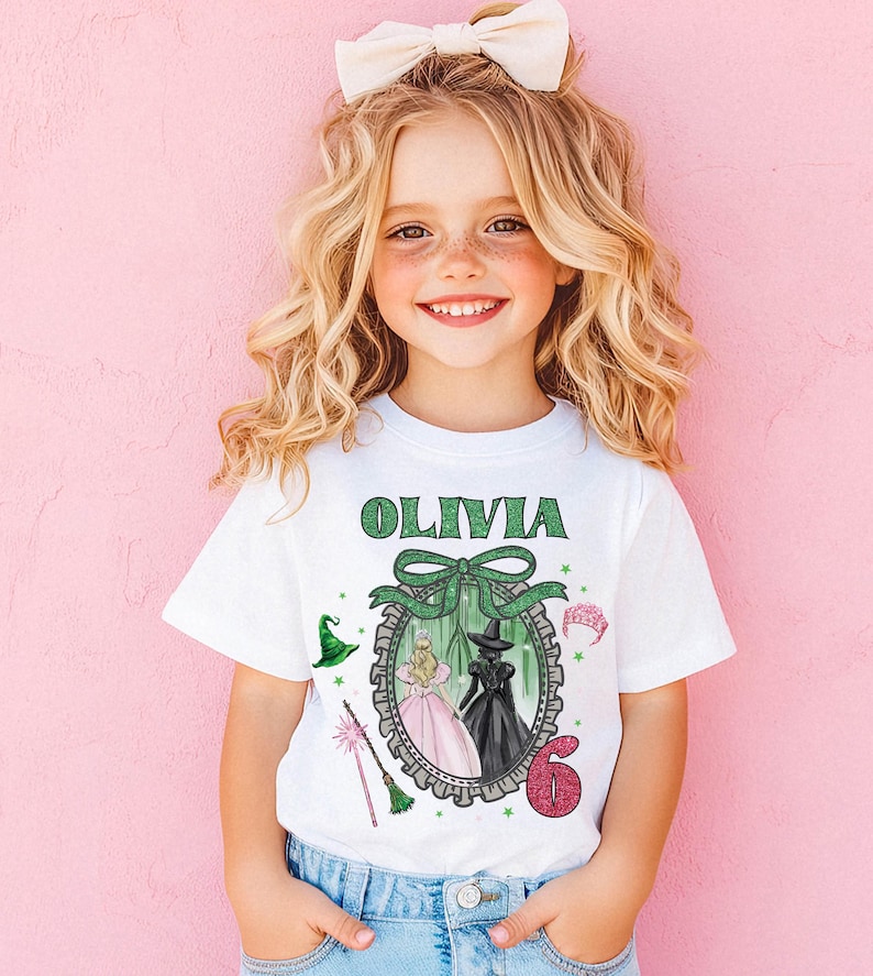 A young girl with curly blonde hair wearing a white t-shirt with a graphic design and a bow on her head, smiling at the camera.