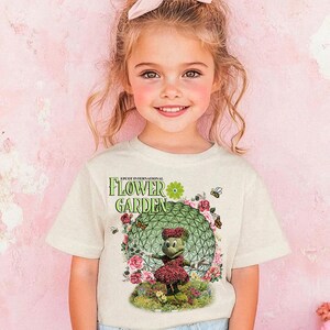 A young girl with a pink bow in her hair is smiling and wearing a t-shirt with a flower garden design.