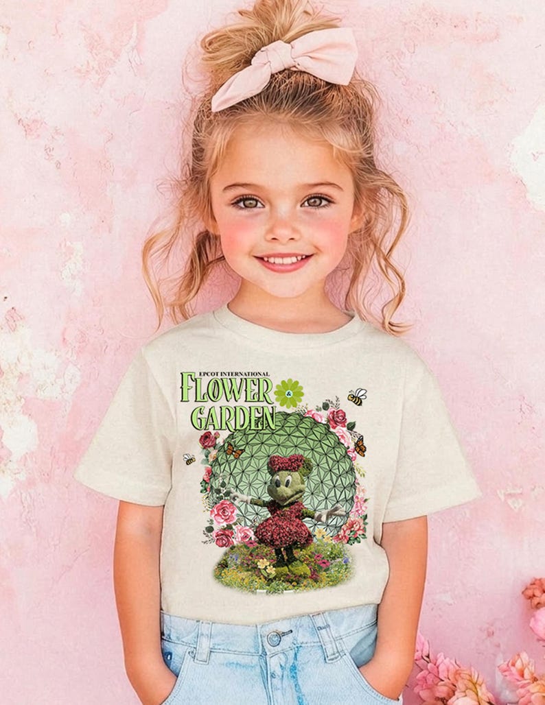 A young girl with a pink bow in her hair is smiling and wearing a t-shirt with a flower garden design.