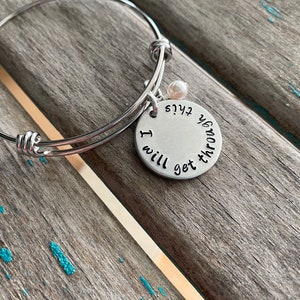 May include: A silver expandable bracelet with a charm that reads "I will get you through this". The charm has a small pearl attached to it.