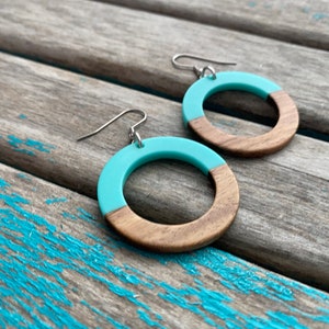 May include: A pair of turquoise and wood hoop earrings. The earrings are made of wood with a turquoise resin coating on the top half of the hoop.