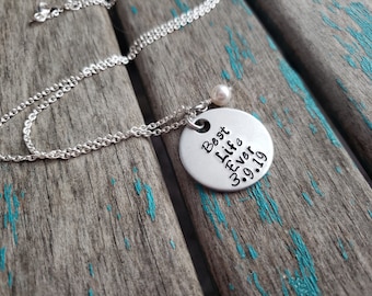 May include: Silver necklace with a round pendant that says "Best Life Ever 3.9.19". The pendant is attached to a silver chain with a small pearl charm.