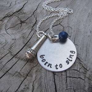 May include: Silver necklace with a microphone charm and a round pendant that says "born to sing". A blue bead is attached to the chain.