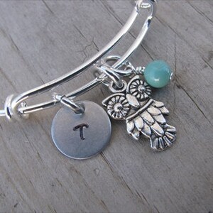 May include: Silver expandable bracelet with a charm of an owl, a turquoise bead, and a silver disc with the letter "T" engraved on it.