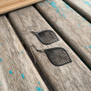 May include: A pair of black dangle earrings with a leaf design. The earrings are made of metal and have a silver hook.
