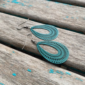 May include: Teal blue dangle earrings with a geometric pattern. The earrings are made of metal and have a hook closure.