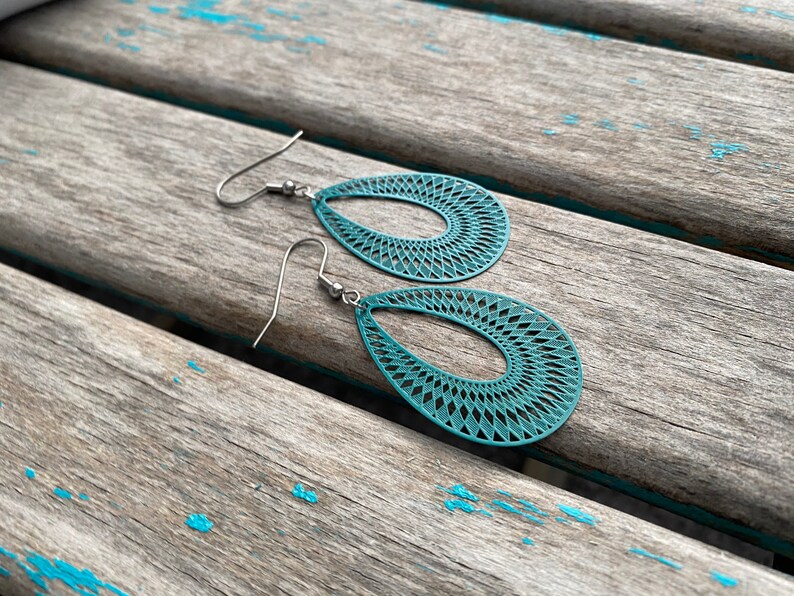 May include: Teal blue dangle earrings with a geometric pattern. The earrings are made of metal and have a hook closure.