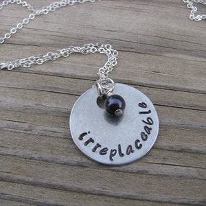 May include: A silver necklace with a round pendant that says "irreplaceable" and a black bead.