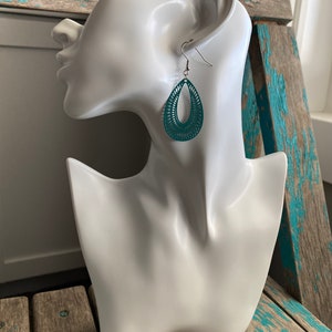 May include: Teal dangle earrings with a geometric design. The earrings are made of metal and have a silver hook.