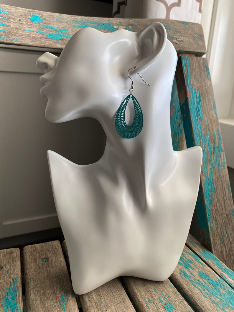 May include: Teal dangle earrings with a geometric design. The earrings are made of metal and have a silver hook.