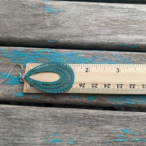 May include: Teal blue dangle earrings with a laser cut design. The earrings are 2 inches long.