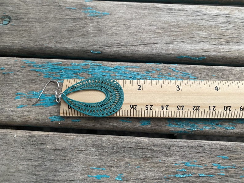 May include: Teal blue dangle earrings with a laser cut design. The earrings are 2 inches long.