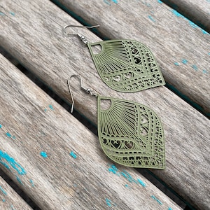 May include: A pair of olive green filigree earrings with a heart design. The earrings are made of metal and have a hook closure.