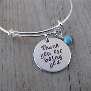 May include: Silver expandable bracelet with a charm that reads "Thank you for being you" and a turquoise bead.