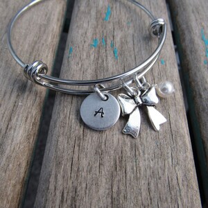 May include: A silver bangle bracelet with a charm that says "A" and a silver bow charm. The bracelet also has a small white pearl charm.