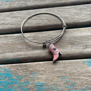 May include: A silver bangle bracelet with a pink boot charm. The boot has a white design and a rhinestone.
