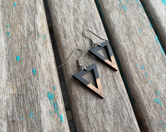 May include: A pair of geometric earrings with a triangle design. The top portion of the triangle is black, while the bottom is a natural wood color. The earrings hang from silver-colored hooks.