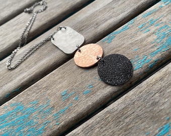 May include: A silver chain necklace with three pendants: a white square, a copper circle, and a black circle.