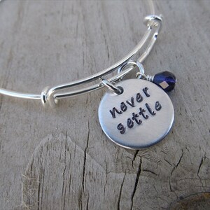 May include: Silver expandable bangle bracelet with a charm that reads "never settle" and a small purple crystal bead.