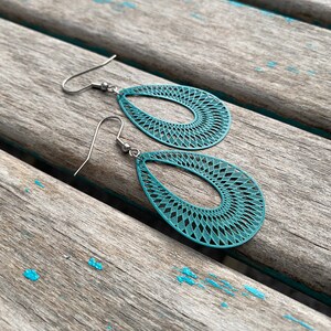 May include: Teal blue dangle earrings with a geometric pattern. The earrings are made of metal and have a hook closure.