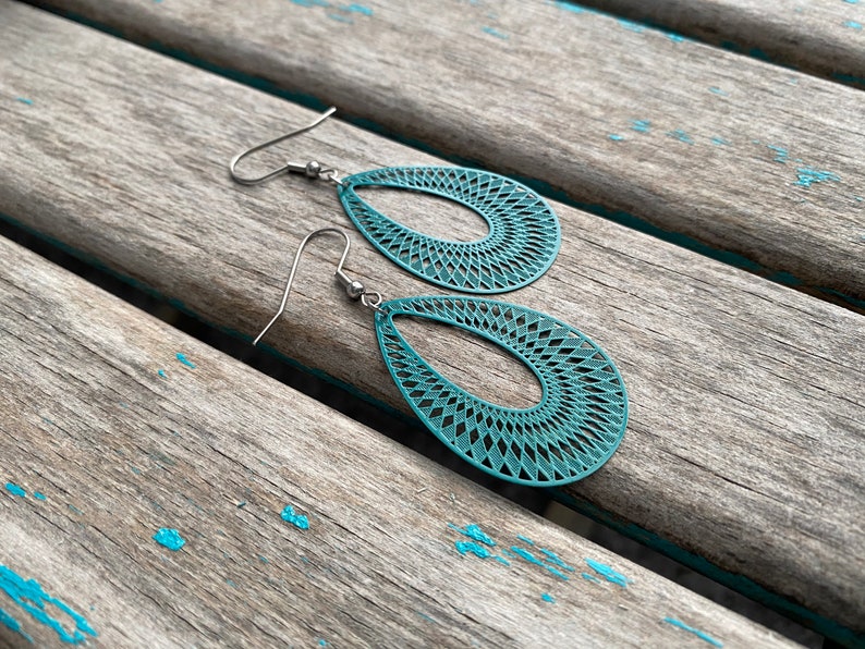May include: Teal blue dangle earrings with a geometric pattern. The earrings are made of metal and have a hook closure.
