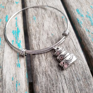 May include: A silver expandable bangle bracelet with a silver charm shaped like a wedding cake.
