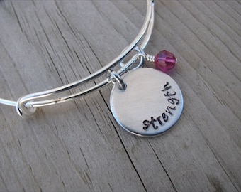 May include: A silver expandable bangle bracelet with a round charm that says "strength" and a pink crystal bead.